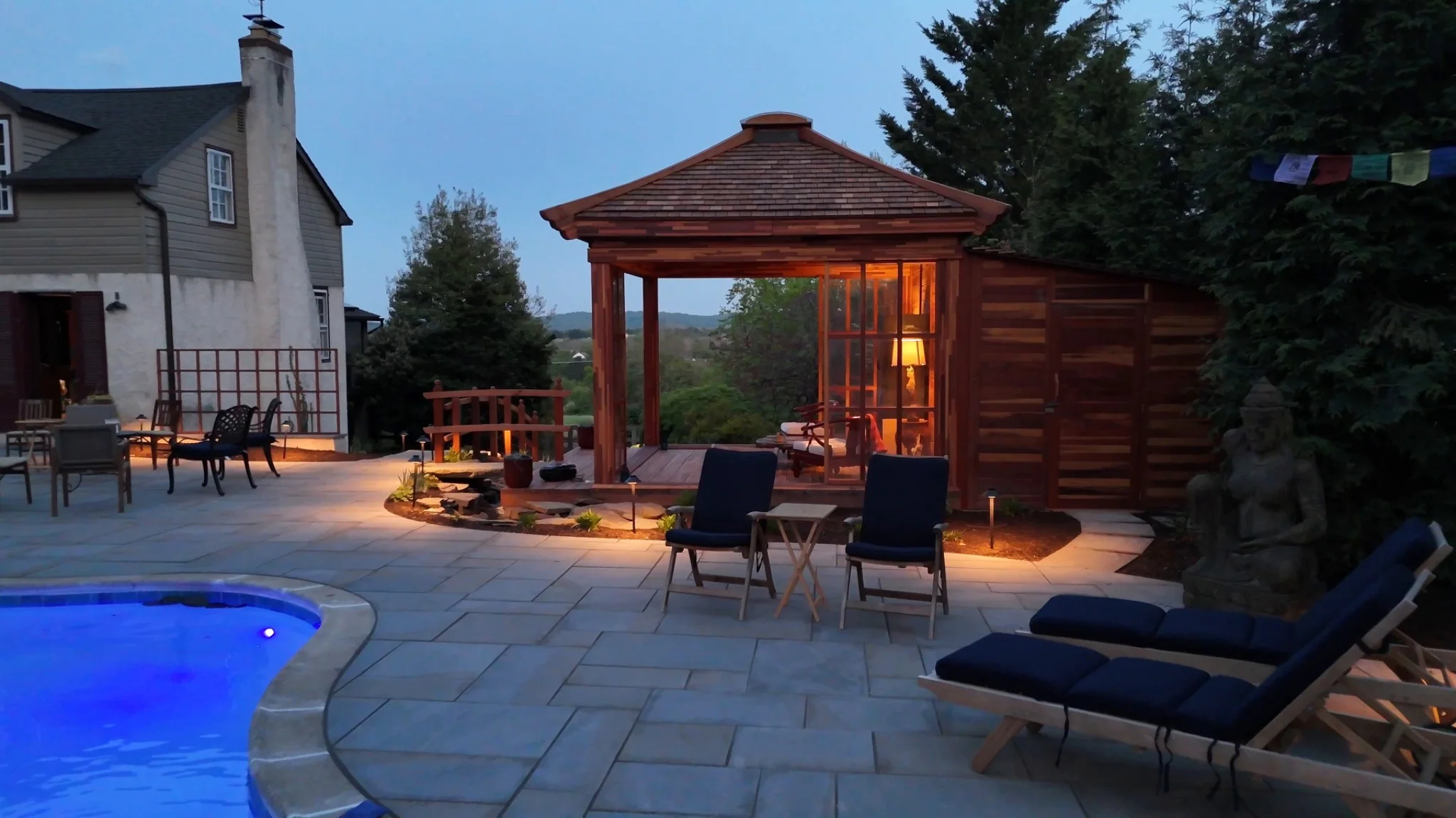 Poolside patio and wood pavilion at twilight with warm landscape lighting